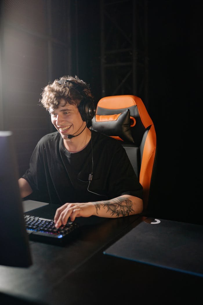 services-01 Smiling young man playing games on PC with headphones, enjoying a thrilling gaming session.
